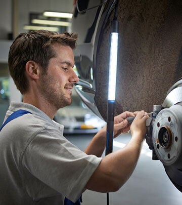 Un hombre se ayuda de una lámpara de trabajo LED para ver más claramente mientras repara un coche